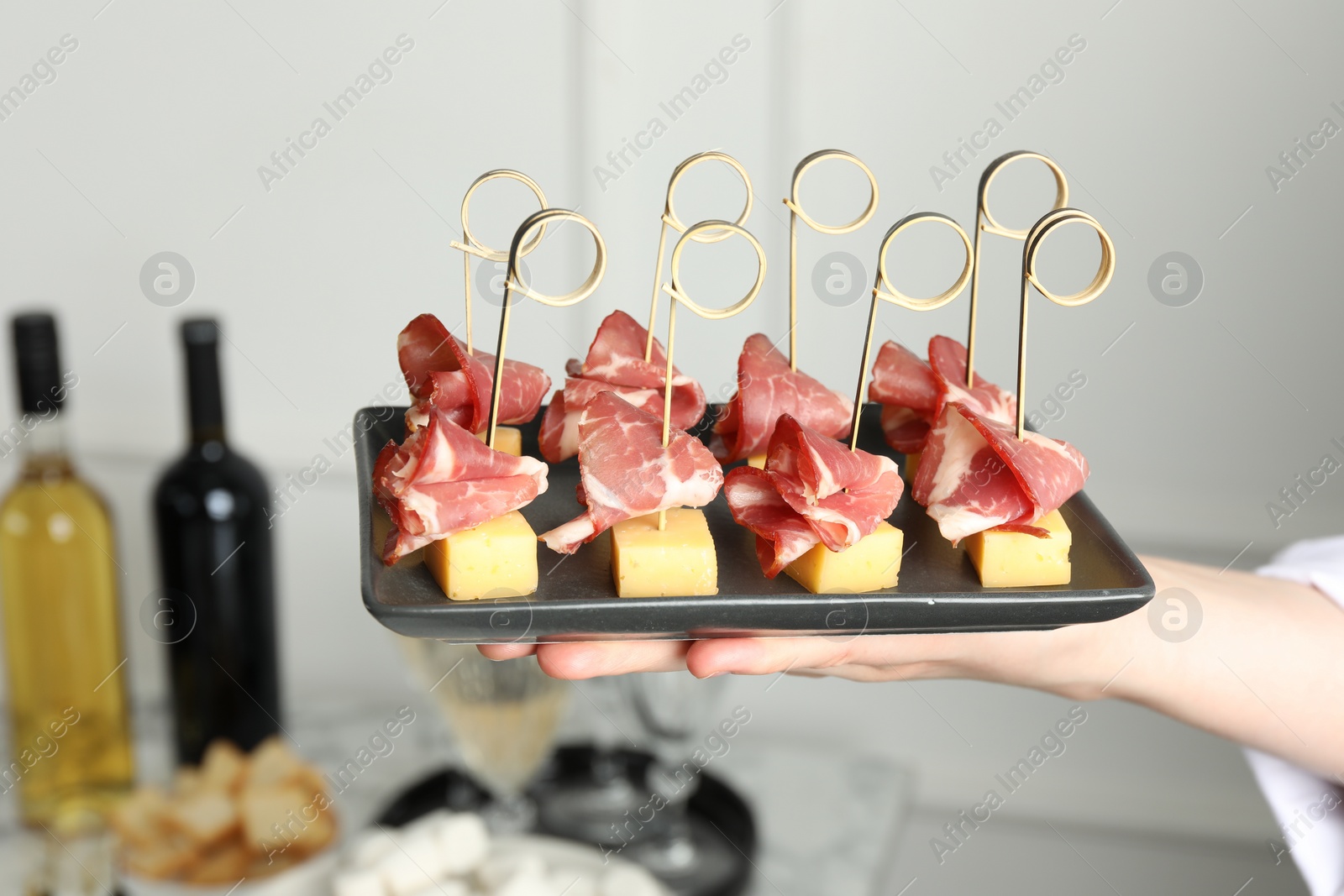 Photo of Woman holding plate of tasty canapes with ham and cheese indoors, closeup