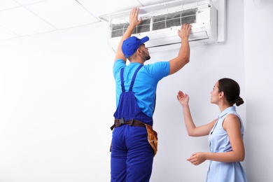 Professional technician speaking with woman about air conditioner indoors