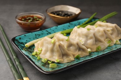 Photo of Delicious gyoza (asian dumplings) with green onions and chopsticks on gray table, closeup
