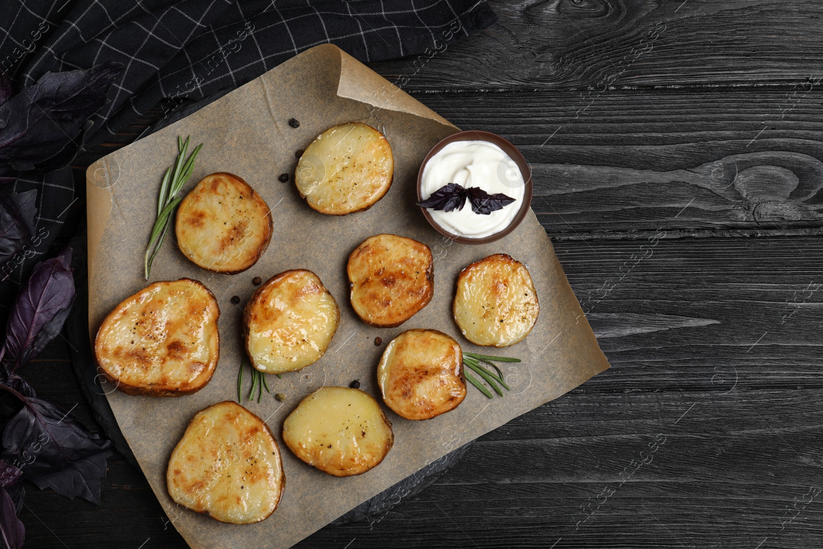 Photo of Delicious potato wedges with sour cream on black wooden table, flat lay