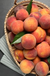 Photo of Fresh peaches and leaves in basket on grey textured table, top view