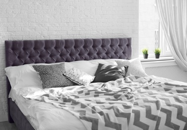 Photo of Bed with pillows and plaid near brick wall. Interior design