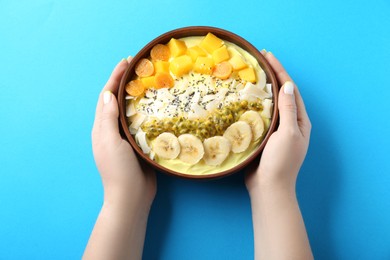 Woman holding tasty smoothie bowl with fresh fruits at light blue table, top view