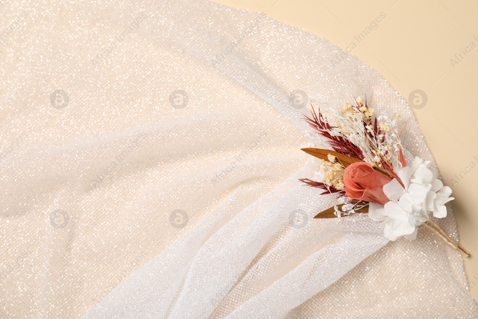 Photo of Stylish boutonniere and white fabric on beige background, top view. Space for text