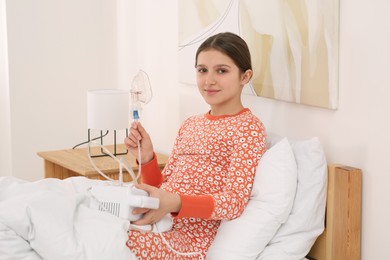 Photo of Cute girl holding nebulizer for inhalation on bed at home
