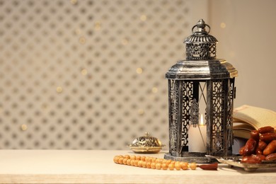 Photo of Arabic lantern, Quran, misbaha and dates on white table. Space for text