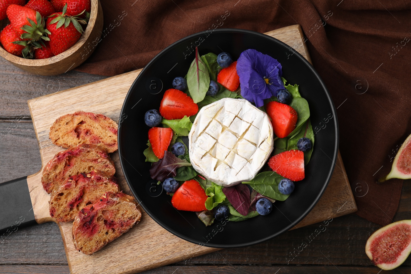 Photo of Delicious salad with brie cheese, blueberries and strawberries served on wooden table, flat lay