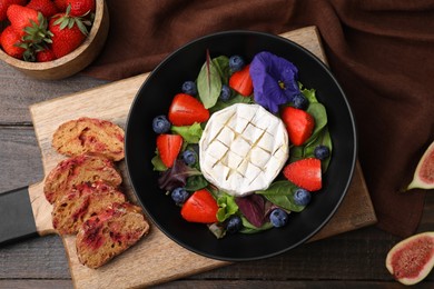 Photo of Delicious salad with brie cheese, blueberries and strawberries served on wooden table, flat lay