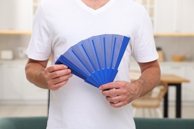 Photo of Man with blue hand fan in kitchen, closeup