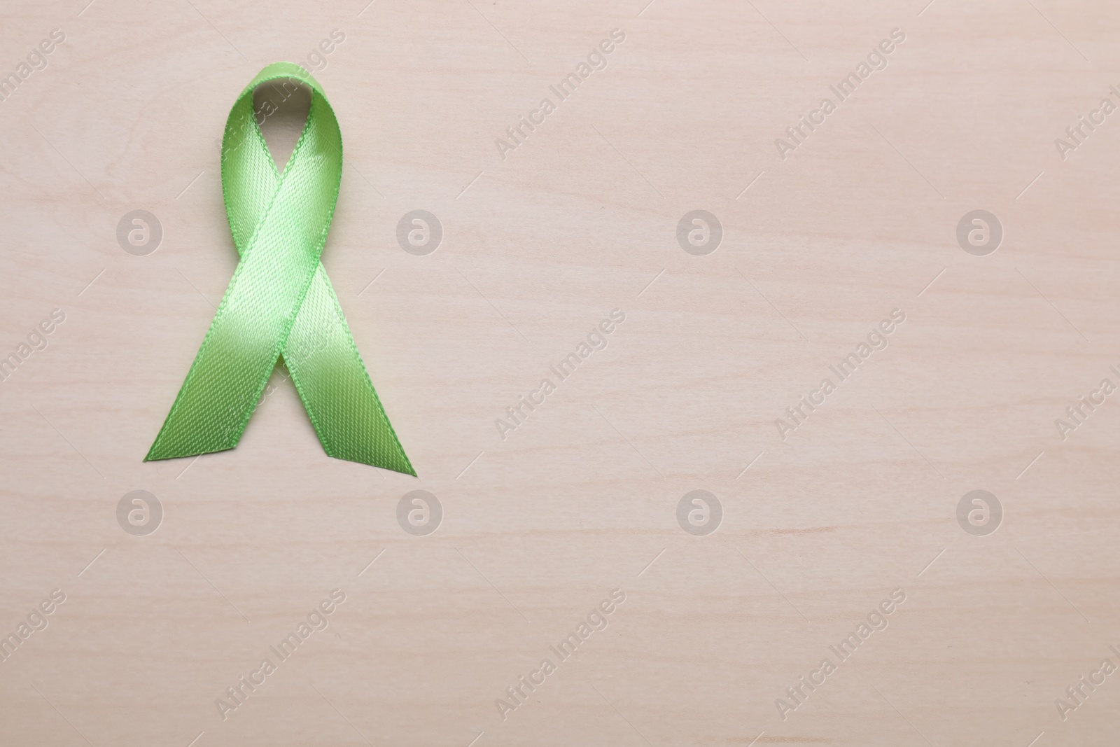 Photo of World Mental Health Day. Green ribbon on wooden background, top view with space for text