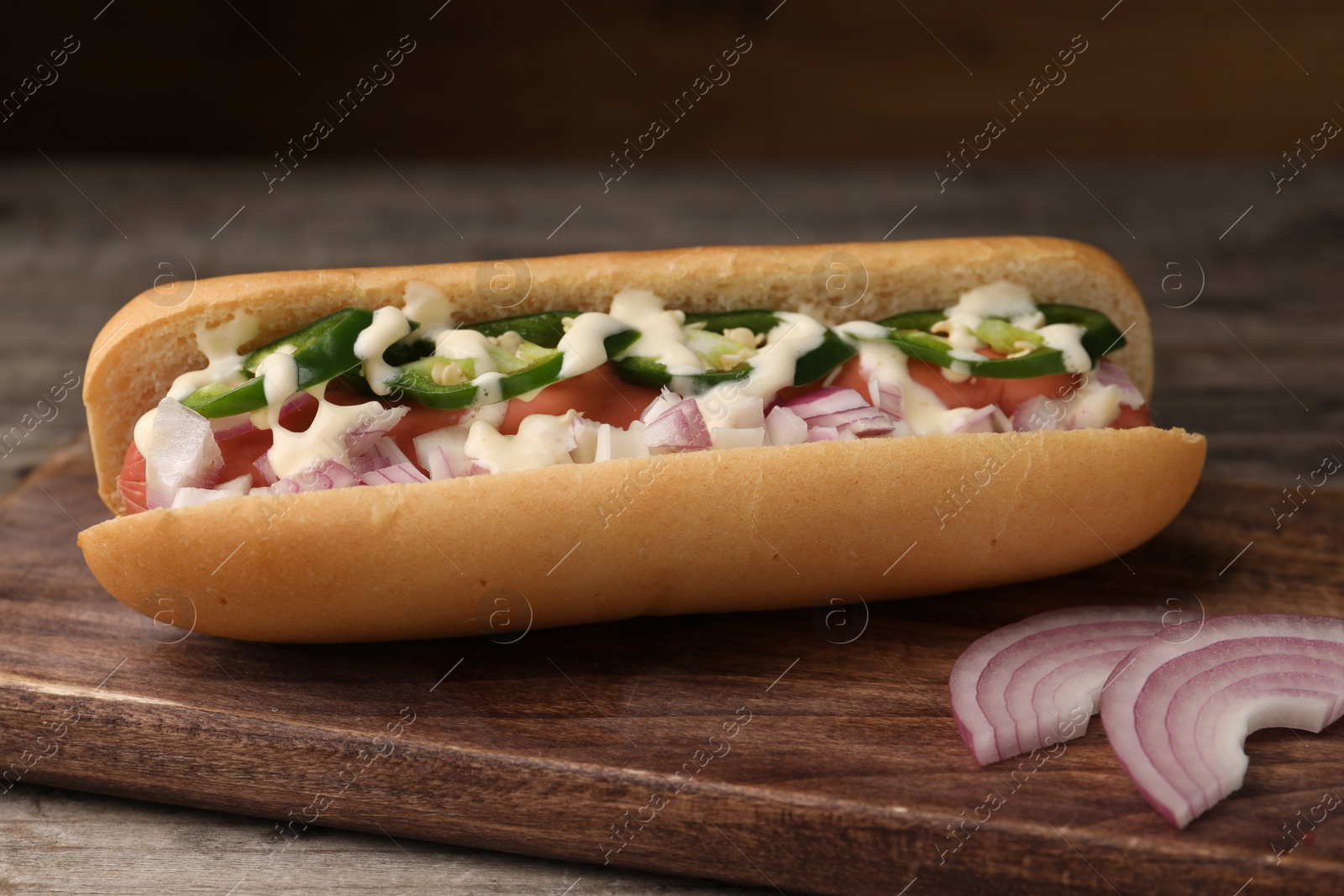 Photo of Delicious hot dog with onion, chili pepper and sauce on wooden table, closeup