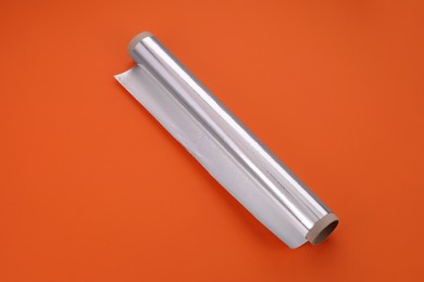 Roll of aluminum foil on orange background, above view