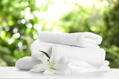 Stack of clean soft towels and flower on table against blurred background