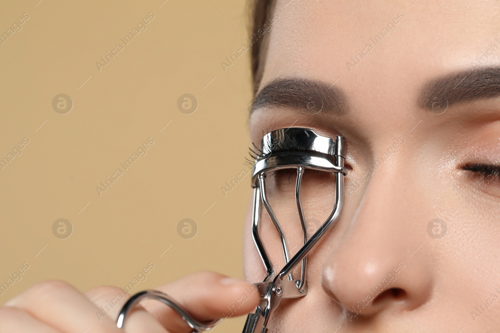 Photo of Woman using eyelash curler on beige background, closeup. Space for text