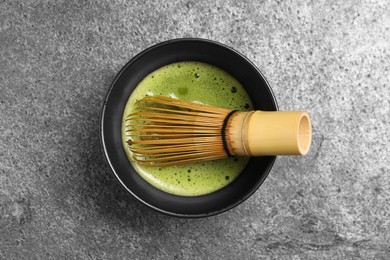 Cup of fresh green matcha tea with bamboo whisk on grey table, top view