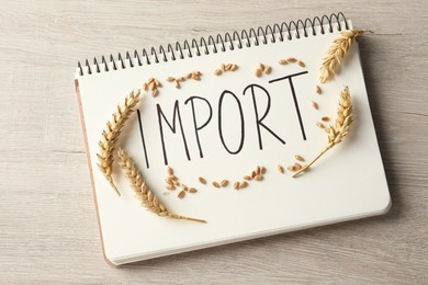 Photo of Notebook with word import and ears of wheat on wooden table, top view