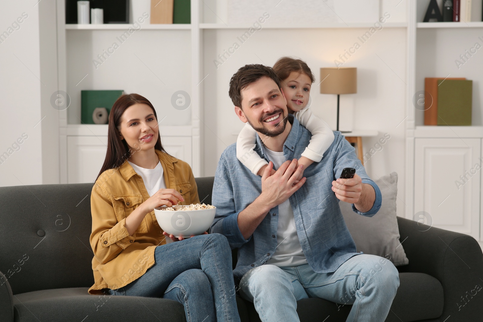 Photo of Happy family watching movie at home. Father changing TV channels with remote control