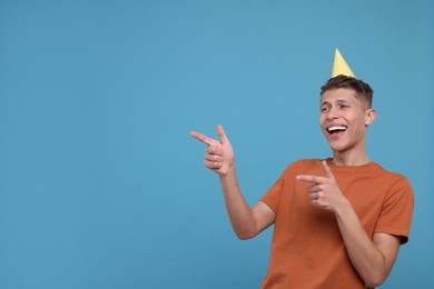 Photo of Happy man in party hat pointing at something on light blue background. Space for text