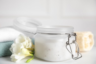 Photo of Jar of salt scrub, freesia flowers and towels on white table