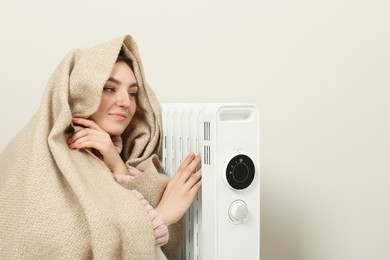 Young woman warming herself near modern electric heater indoors