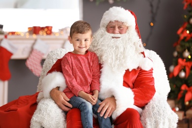 Photo of Little boy sitting on authentic Santa Claus' lap indoors