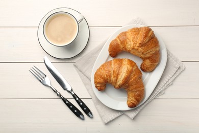 Delicious fresh croissants served with coffee on white wooden table, flat lay