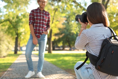 Photo of Young female photographer taking photo of man with professional camera in park
