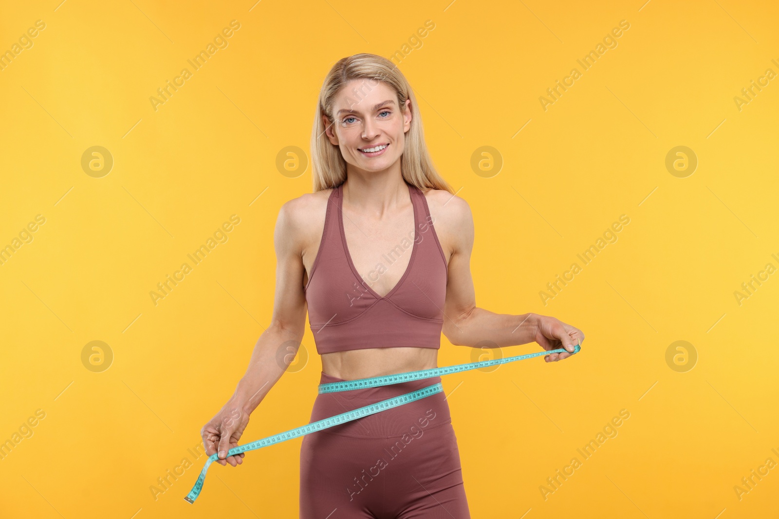 Photo of Slim woman measuring waist with tape on yellow background. Weight loss