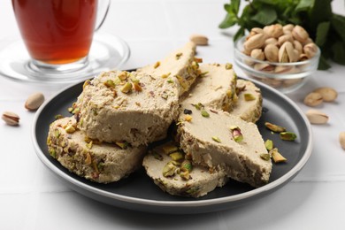 Photo of Tasty halva with pistachios served on white tiled table, closeup