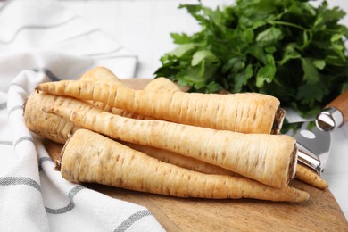 Photo of Whole raw parsley roots and fresh herb on white table, closeup