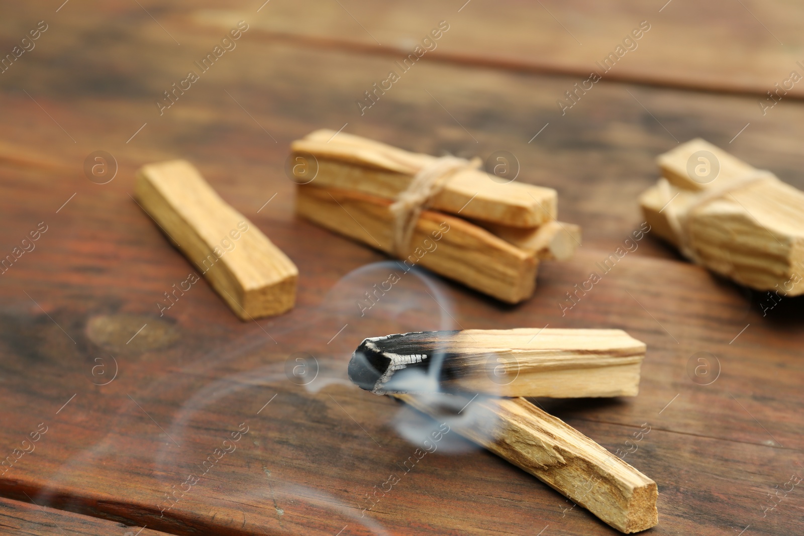 Photo of Palo Santo stick smoldering on wooden table, closeup