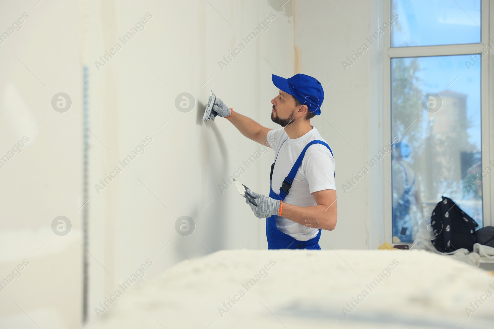 Photo of Professional worker plastering wall with putty knives indoors