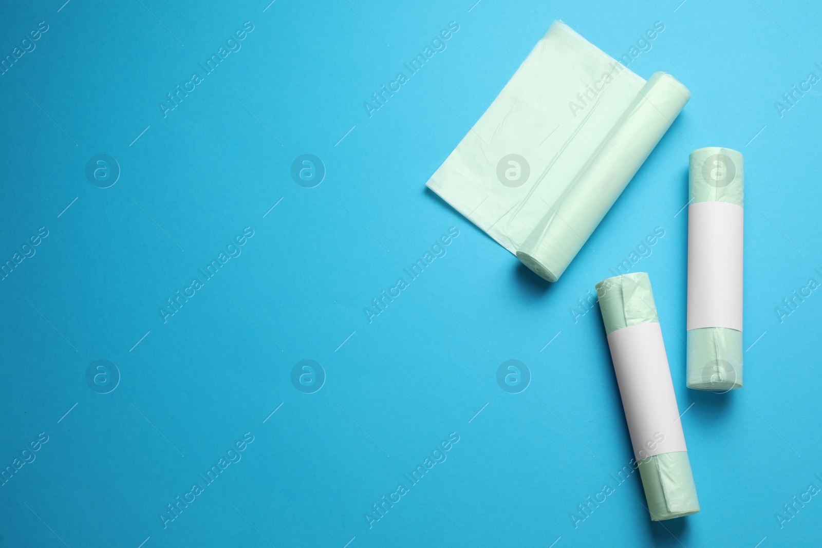 Photo of Rolls of different garbage bags on light blue background, flat lay. Space for text