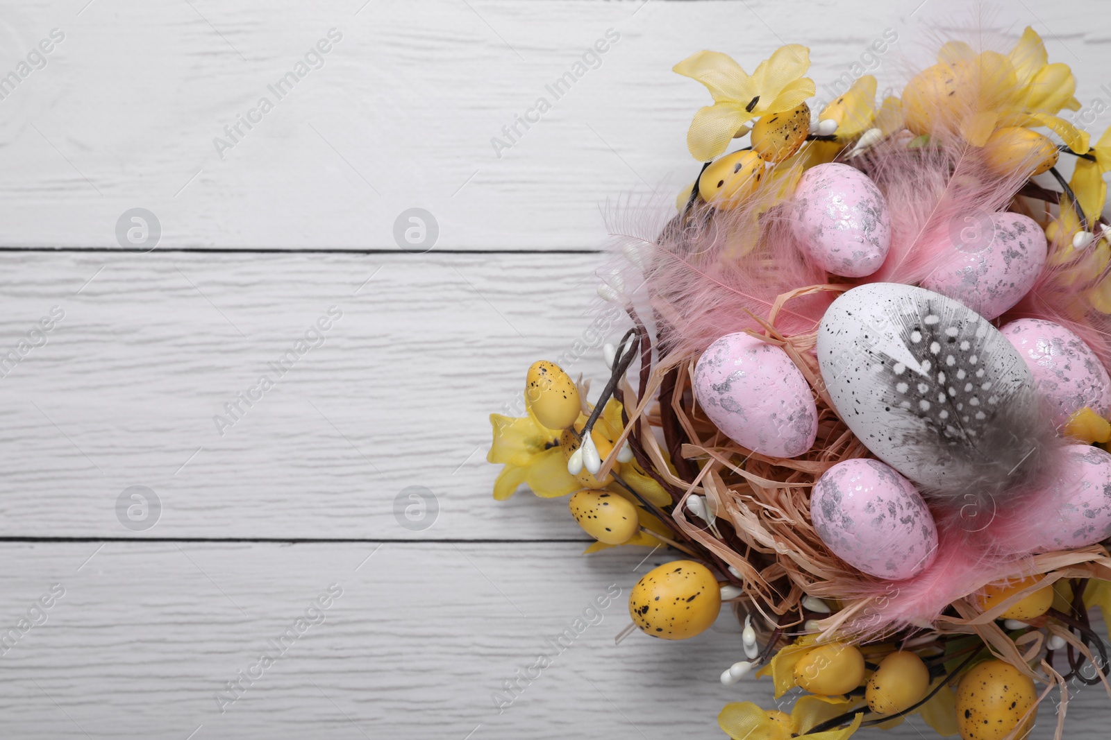 Photo of Festively decorated Easter eggs on white wooden table, top view. Space for text