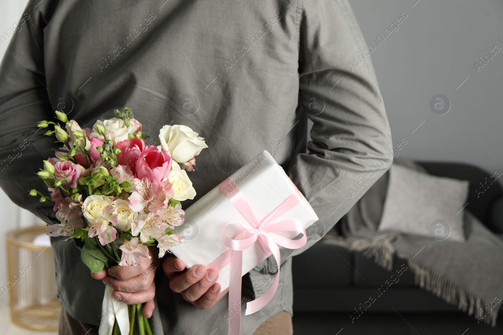 Photo of Man hiding bouquet of flowers and present indoors, closeup