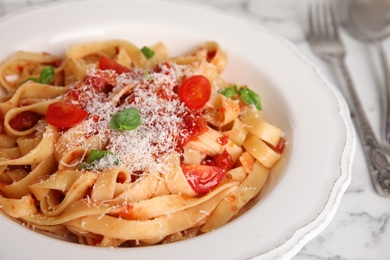 Tasty pasta with tomatoes, cheese and basil on white marble table, closeup