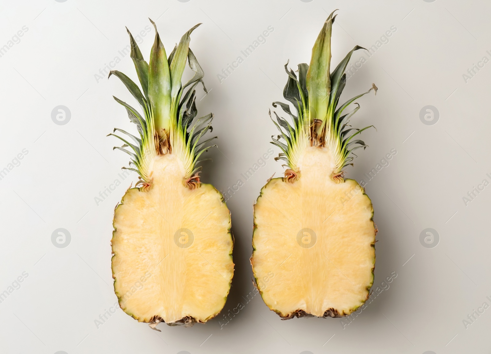 Photo of Fresh pineapple halves on light background, top view