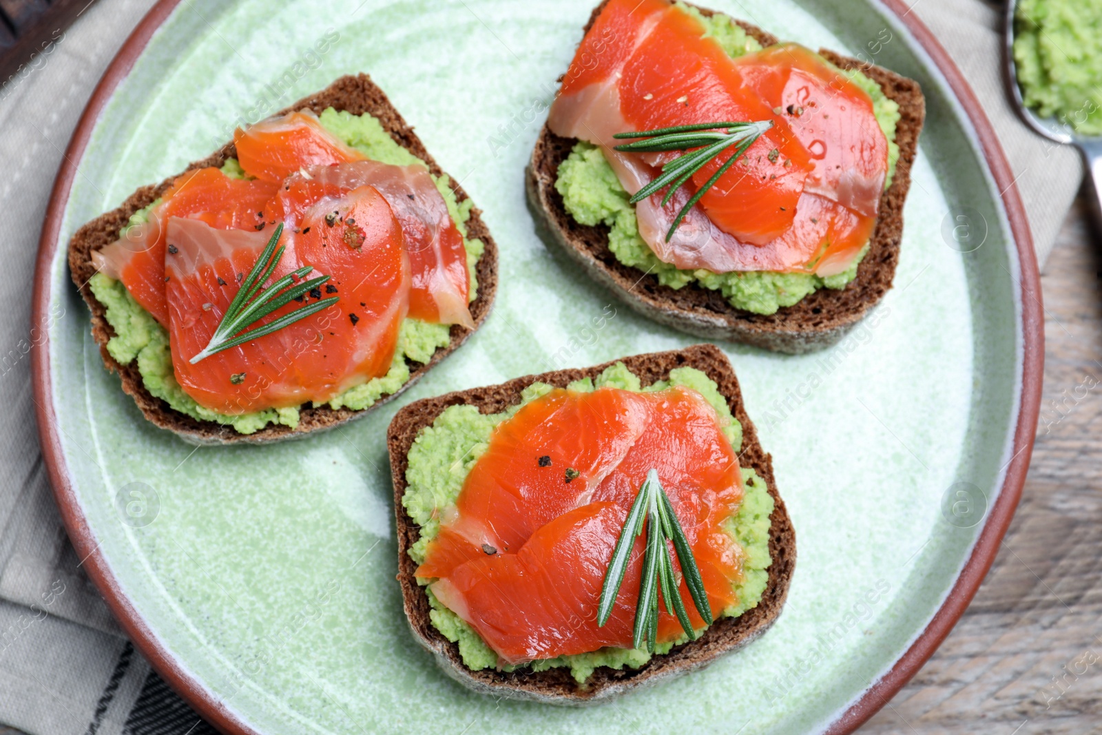 Photo of Delicious sandwiches with salmon, avocado and rosemary on plate, top view