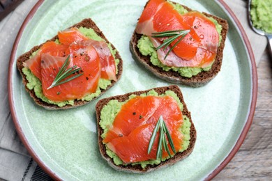 Delicious sandwiches with salmon, avocado and rosemary on plate, top view