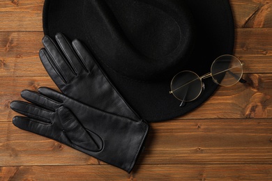 Stylish black leather gloves, hat and glasses on wooden table, flat lay