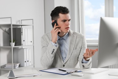 Photo of Confused businessman talking on phone while working in office