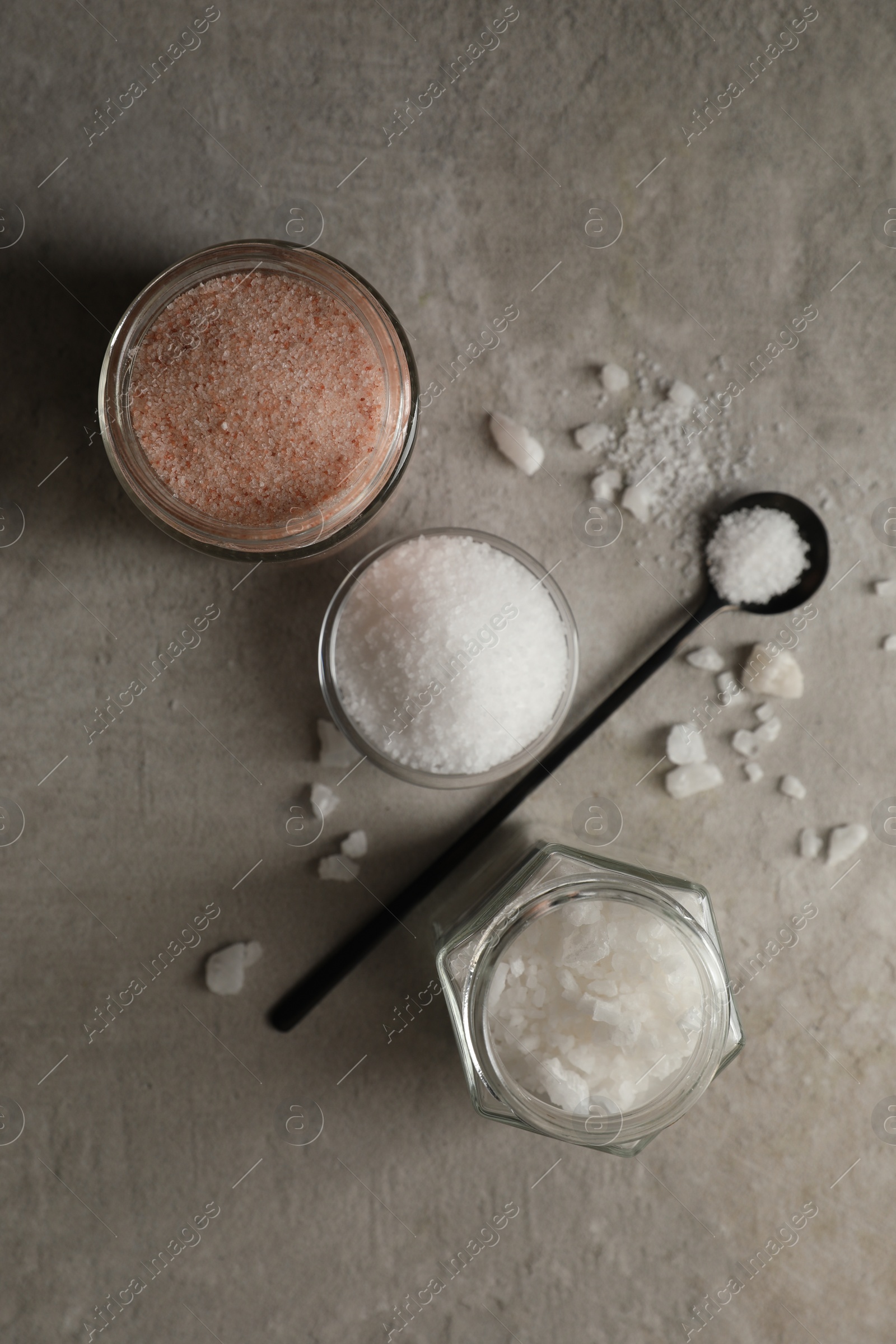 Photo of Different natural salt on grey textured table, flat lay