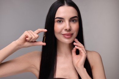 Photo of Beautiful young woman holding skincare ampoule on grey background