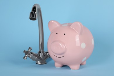 Photo of Water scarcity concept. Piggy bank and tap on light blue background