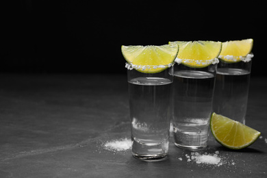 Photo of Mexican Tequila shots, lime slices and salt on black table. Space for text