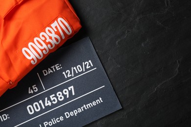 Mugshot letter board and prison uniform on black table, flat lay. Space for text