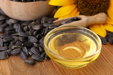 Photo of Sunflower oil in glass bowl and seeds on wooden table, closeup