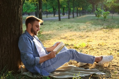 Photo of Young man reading book on green grass near tree in park