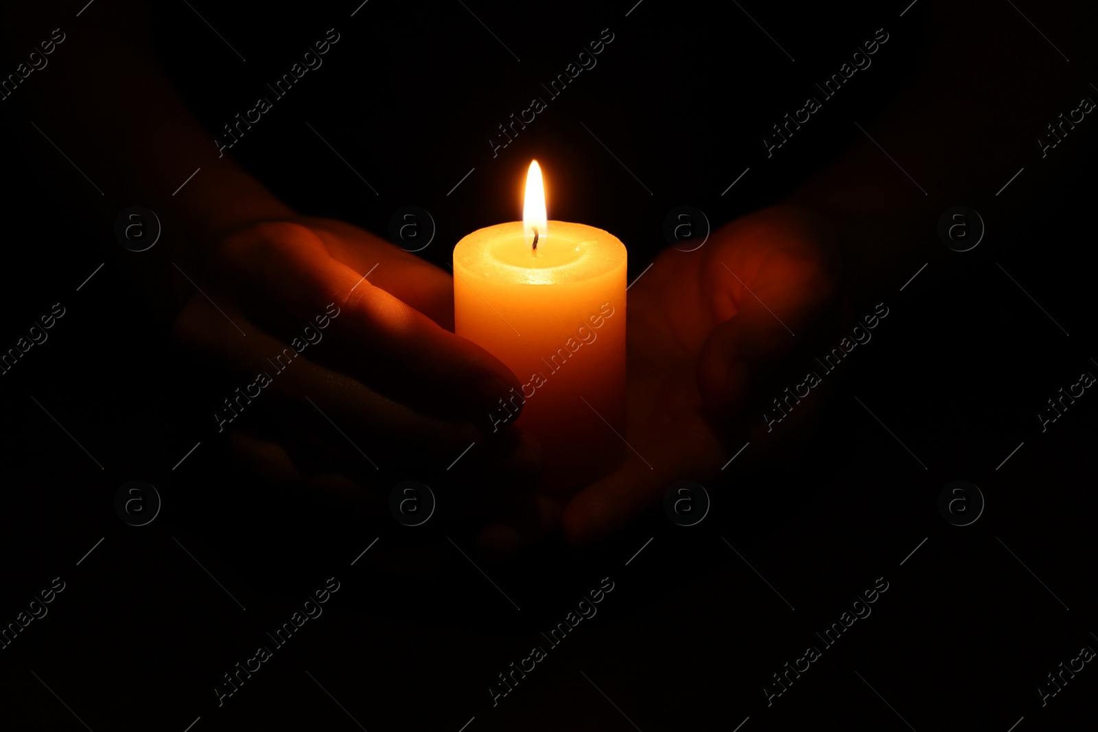 Photo of Woman holding burning candle in hands on black background, closeup