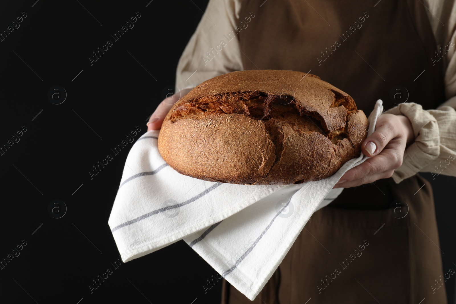 Photo of Woman holding freshly baked bread on black background, closeup